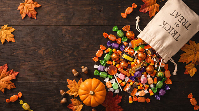 Trick or treat sack with spilled colorful hard candies, acorns and maple leaves on dark wood
