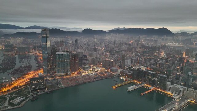 Low cloud draped over the mountains behind Kowloon at sunrise, slow sideways drone shot past the skyscraper and the dense residential districts of West Kowloon, Hong Kong