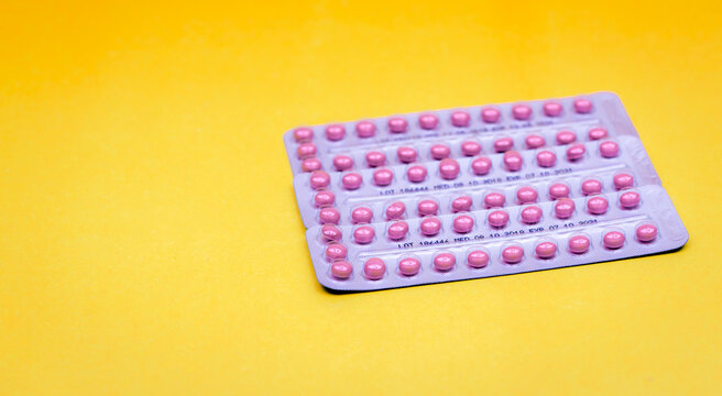 Contraceptive pills in three blister packs on a yellow surface, pink oral medication for birth control and family planning, pharmaceutical packaging for reproductive health and hormone treatment.
