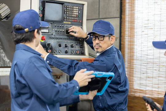 製造工場で工作機械の操作方法を若手男女従業員に指導するベテラン男性技術者