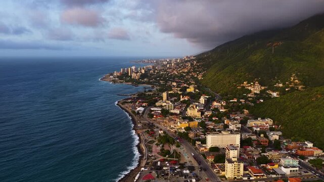 A stunning aerial perspective of a coastal South American city nestled between lush green mountains and the blue Caribbean sea during sunset. Ideal for travel and real estate content.