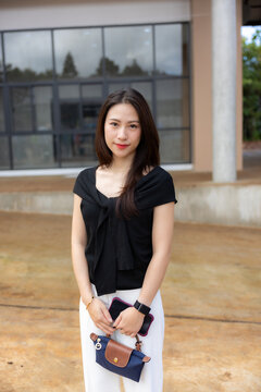 Asian woman portrait wearing black blouse and holding handbag outdoors near modern building, calm expression and natural light