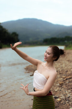 Young Asian woman in traditional clothing posing beside mountain lake with joyful expression and natural landscape