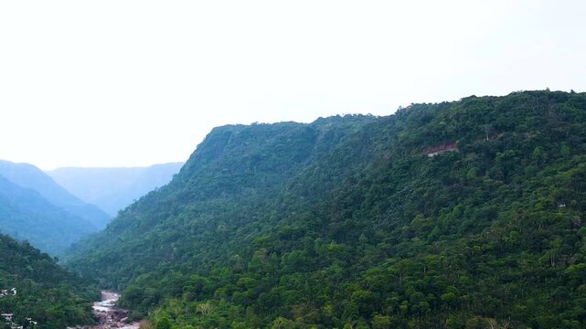 A river flowing through a mountainous landscape with green hills and natural vegetation in Bangladesh India borderland