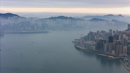 Fototapeta premium Aerial drone view of the eastern end of Hong Kong Island at dawn, with misty mountains behind Kowloon, a wide empty harbour and the city clinging to the narrow shoreline