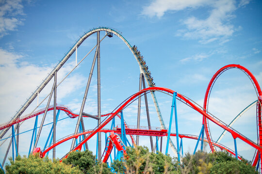 Steel roller coaster tracks with riders descending against bright blue sky