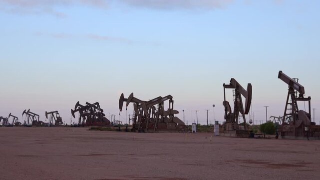 Line of Petroleum Pump Jacks Pumping in Desert Oil Field During Morning Hours