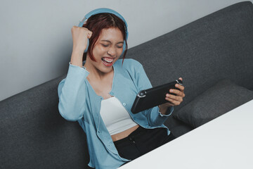Excited young Asian woman is using headphones and handheld console game playing online games. © ChristyMerry