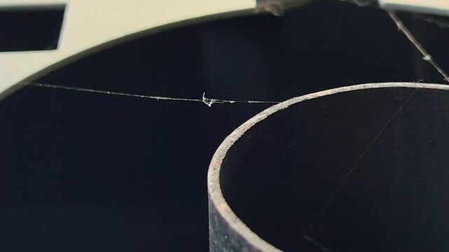 Close-up shot of spider silk string or web thread swaying on industrial machinery.