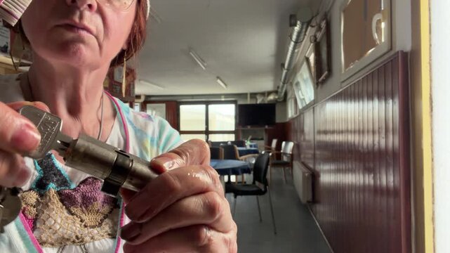 Close-up of a woman holding a door lock cylinder while turning and removing the key to check the mechanism. She uses a toothbrush while inspecting and cleaning the cylinder. Static shot