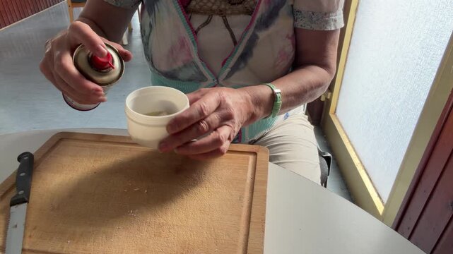 Close-up of a woman spraying cleaning liquid onto a removed door lock cylinder placed inside a plastic container. The fluid is used to loosen and wash away accumulated dirt. Static shot