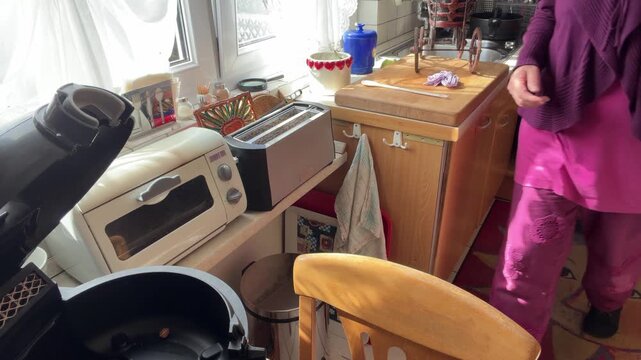 Woman unplugs an air fryer from the power outlet and carries the appliance away from the kitchen counter. A doll carriage is visible in the background during the household activity. Static shot