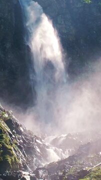 Waterfall spray illuminated by bright sunlight. Waterfall mist above a rocky stream. Sunlit waterfall against a shadowed cliff face. Dramatic waterfall with swirling clouds of mist.