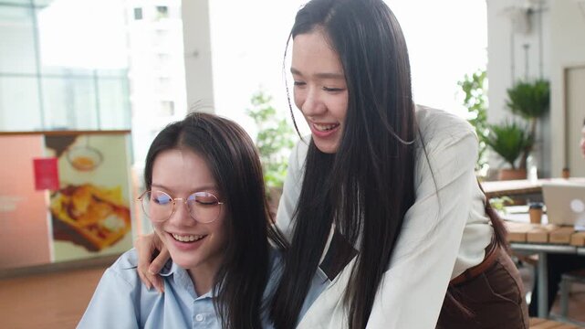 Two Asian Businesswomen Collaborating and Laughing Over Laptop in Modern Office