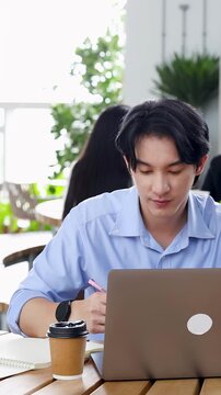 Asian Businessman Working on Laptop and Taking Notes in Modern Coworking Space