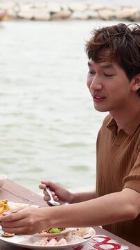Asian Man Eating Seafood at Seaside Restaurant Table