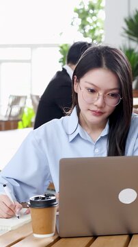 Asian Businesswoman Working on Laptop and Taking Notes in Modern Office