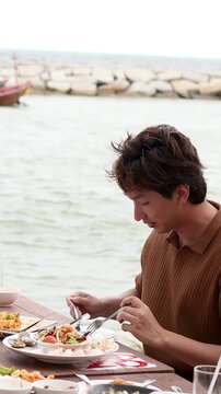 Asian Man Eating Seafood at Seaside Restaurant