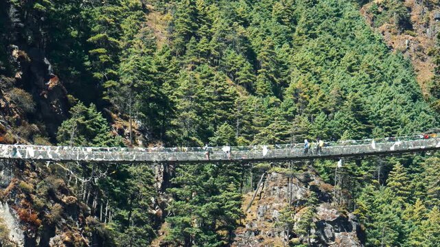 Courageous hikers and trekkers crossing the famous high hillary suspension bridge, surrounded by the breathtaking himalayan mountains and dense green forests on the trail to everest base camp