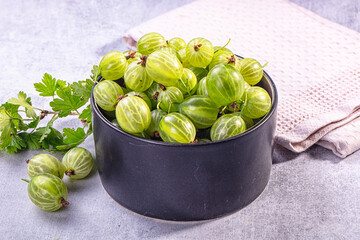 Fresh green gooseberries in black ceramic bowl with leaves on light gray surface © Andrei Starostin