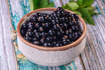 Fresh black currants in ceramic bowl on rustic wooden surface © Andrei Starostin