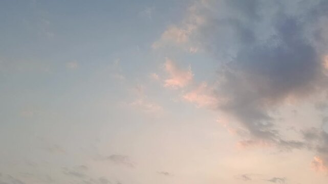 Dramatic evening sky with soft clouds illuminated by warm sunset light, creating a peaceful natural background with changing colors and atmospheric cloud formations.