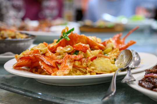 Cantonese-style lobster with e-fu noodles (or yi mein) on a plate. Unrecognizable people dining in the restaurant.