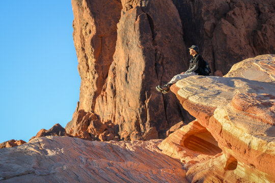 Tourist sitting on the red rocks in the afternoon sun, enjoying the beautiful views. Valley of Fire State Park. Nevada, USA.