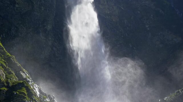 Waterfall crashing onto wet jagged rocks. Waterfall flowing through a steep rocky gorge. Rushing waterfall water cascading between boulders. Powerful waterfall spray above the rocky base.