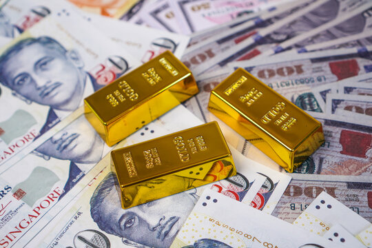 Three fine gold bullion bars arranged in a triangular cluster at the center over a full frame scattered multi currency backdrop.
