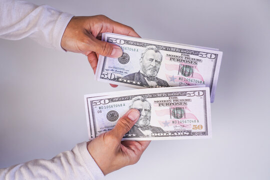 A person's hands holding and comparing two separate fifty dollar banknotes against a plain white background.