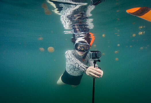 Woman filming herself snorkeling with golden jellyfish