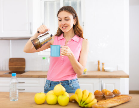 Young woman pouring coffee from percolator into cup in home kitchen