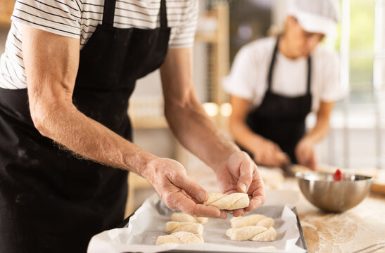 Close-up of baker hands placing pieces of raw dough on baking sheet in oven