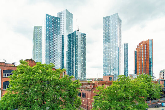Modern futuristic architecture rises above green trees in Manchester