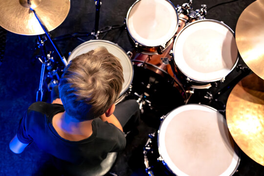 A boy plays a drum kit indoors