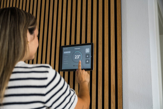 Woman adjusts temperature on smart home tablet on the wall