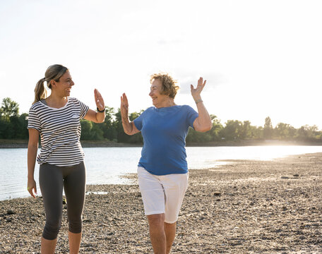 A woman and a senior share a high five during a walk by the river