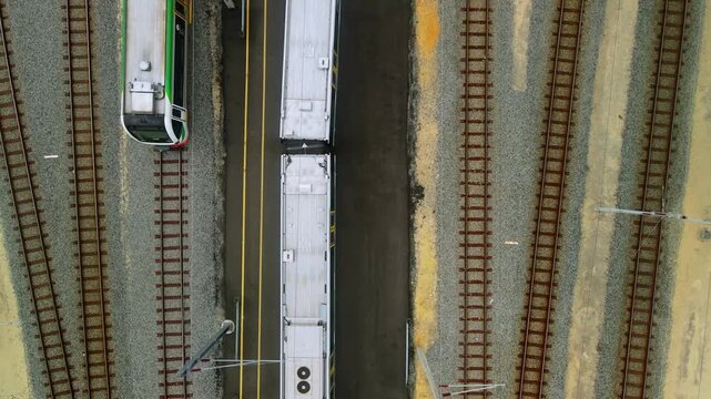 Top down view of a stationary commuter train positioned between parallel rail tracks at a railway depot