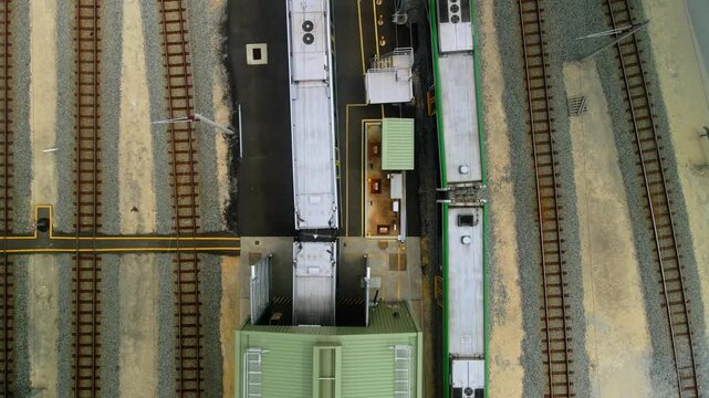 Top down view of two parked commuter trains flanking a maintenance shed between parallel rail tracks