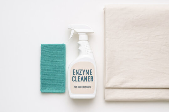 Enzyme cleaner spray bottle with microfiber cloth and folded bed sheet on white background for pet odor removal and household cleaning
