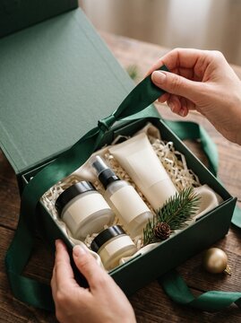 Hands untying ribbon on green gift box with skincare set