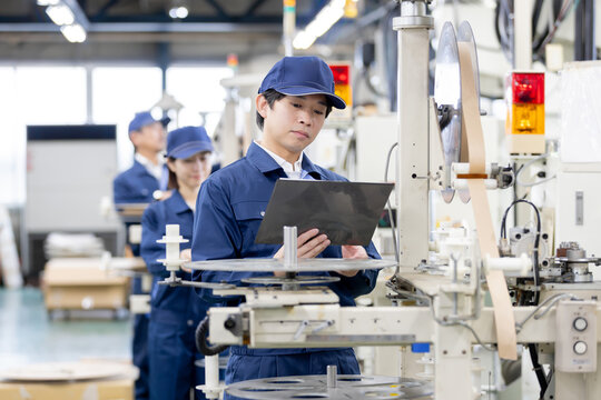 製造工場でタブレット端末を使いながら生産設備の稼働状況を確認する日本人の若い男性作業員