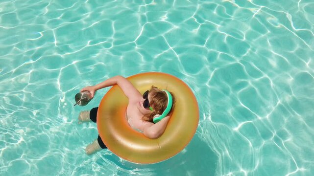 Child relaxing on an inflatable pool ring. Child wearing headphones and sunglasses in water. Floating child holding a drink with straw. Carefree child enjoying summer pool relaxation.
