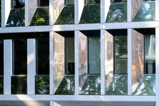 Glass facade with reflections of trees across modern windows creates a geometric architecture pattern on the building as the reflections continue across the windows