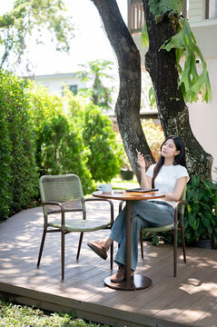 Asian Woman Sitting at Garden Patio Table with Tablet and Stylus