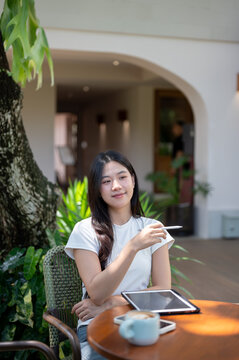 Asian Woman with Tablet and Coffee Gesturing with Stylus Outdoors