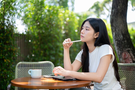 Asian Woman Leaning on Hand Thinking with Stylus at Garden Table