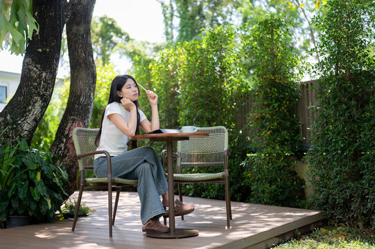 Asian Woman Leaning on Table Daydreaming with Stylus Outdoors