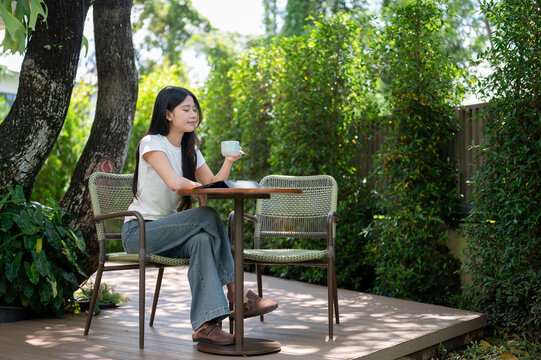 Asian Woman Drinking Coffee with Eyes Closed at Garden Cafe Table